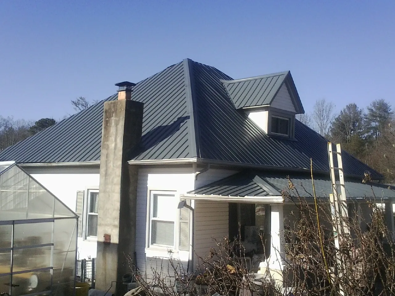 Dark blue standing seam metal roof on a white farmhouse with dormer — Slate & Tile Roof Repair by Roofing Brothers in Ypsilanti