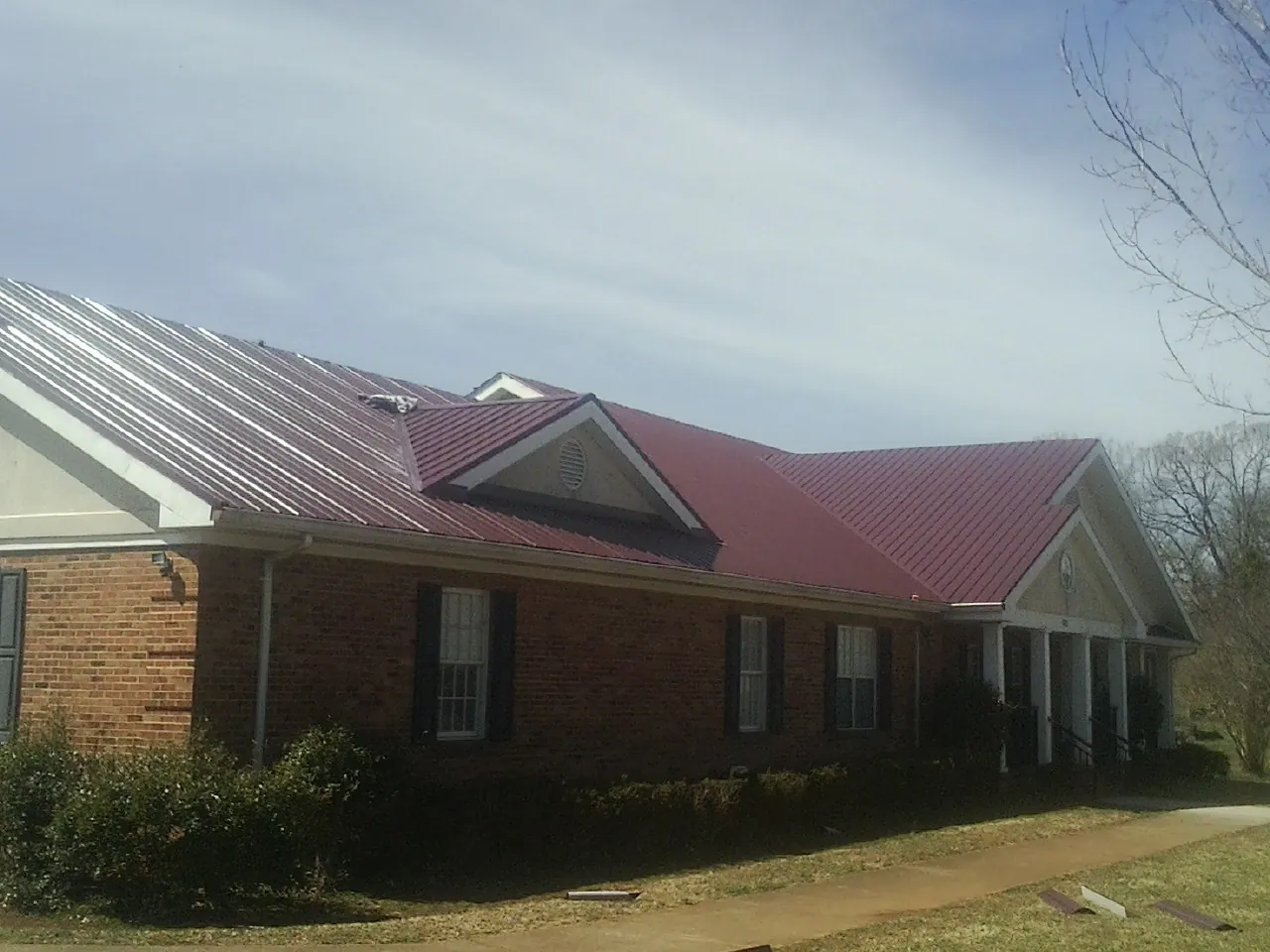 Red metal roof with gabled entries on a long brick building, from a Hail Damage Roof Repair job in Ypsilanti
