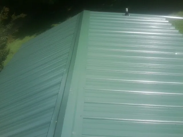 New green metal panels meeting at the ridge of a roof — Flat Roof Repair work by our crew in Ypsilanti