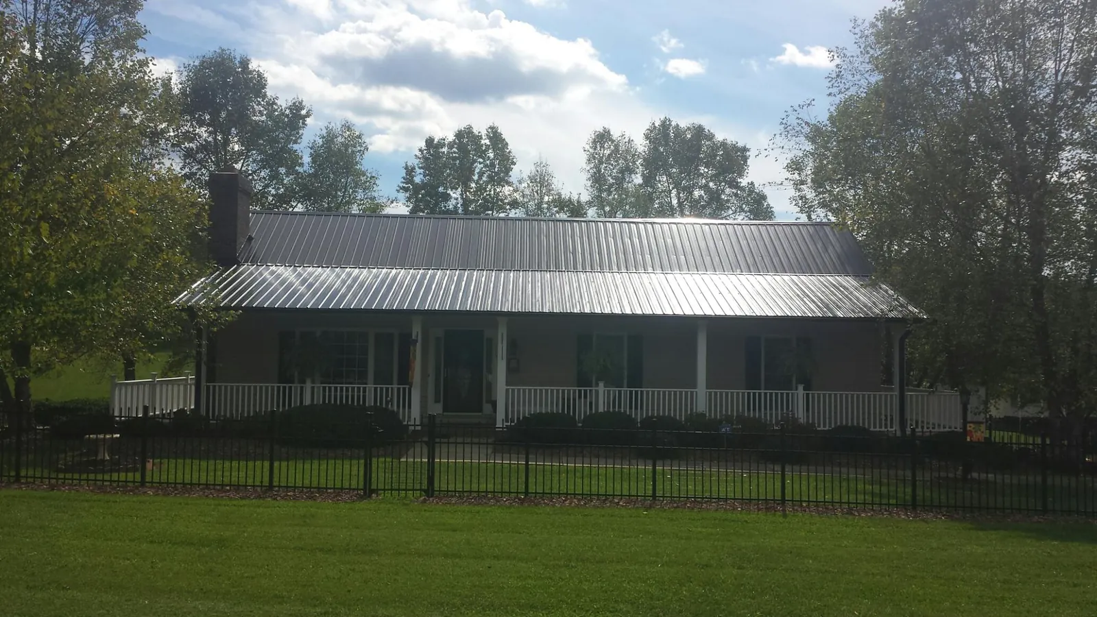 Gray metal roof on a brick ranch with a full width front porch — Gutter Guard Installation work by our crew in Ypsilanti