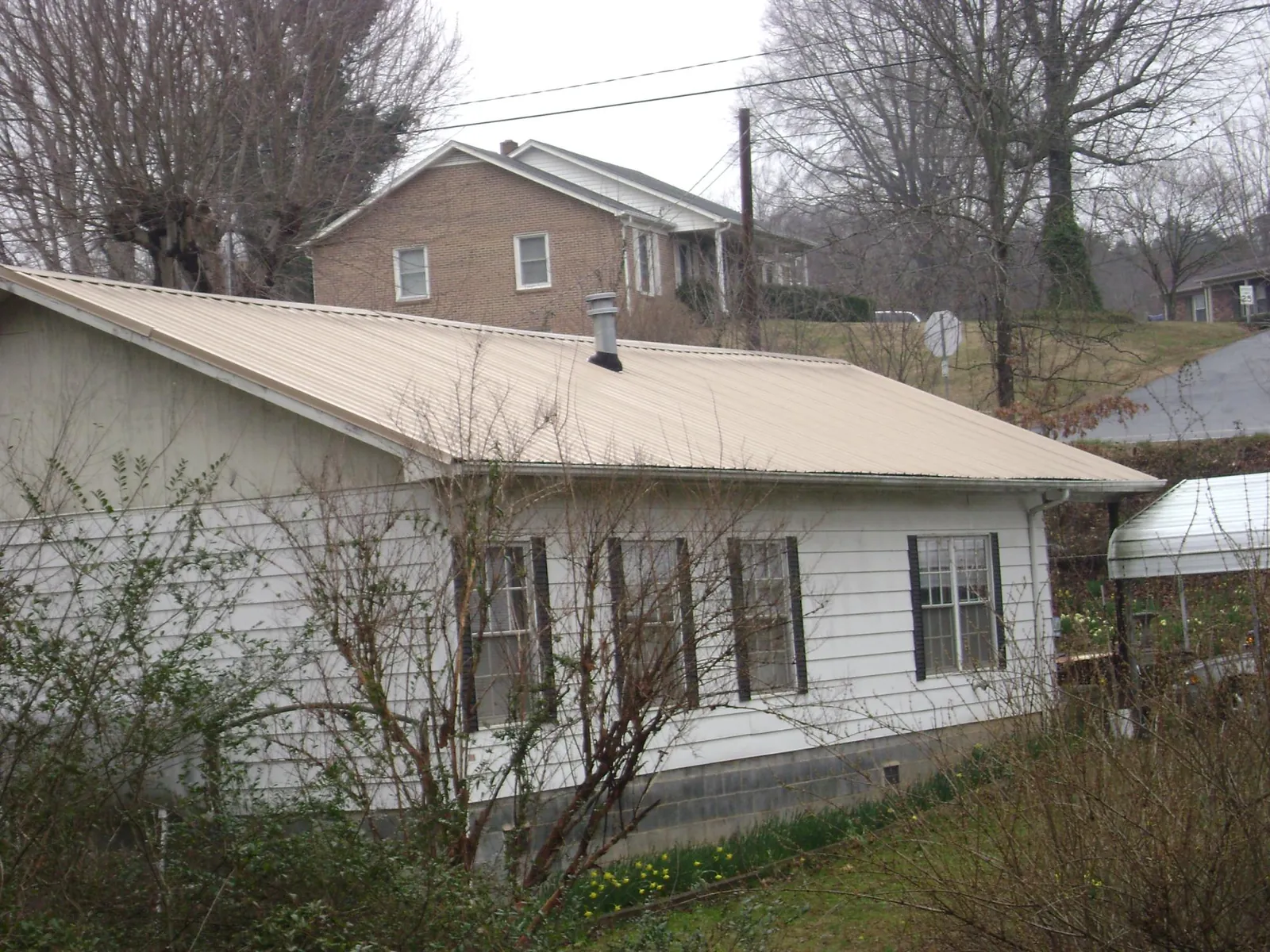 Tan metal roof on a white sided house set into a hillside — Commercial Roofing by Roofing Brothers in Ypsilanti