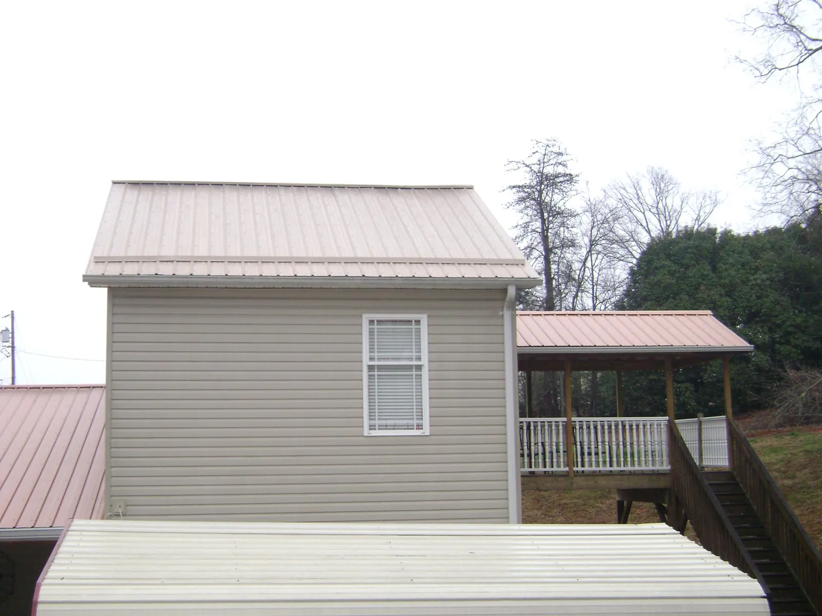Tan metal roofs on a two story addition and attached porch, from a Roof Replacement job in Ypsilanti